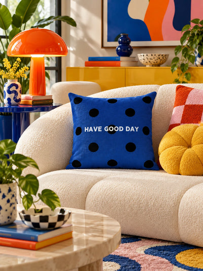 navy polka dot slogan pillow on a curved boucle sofa beside a yellow flower cushion