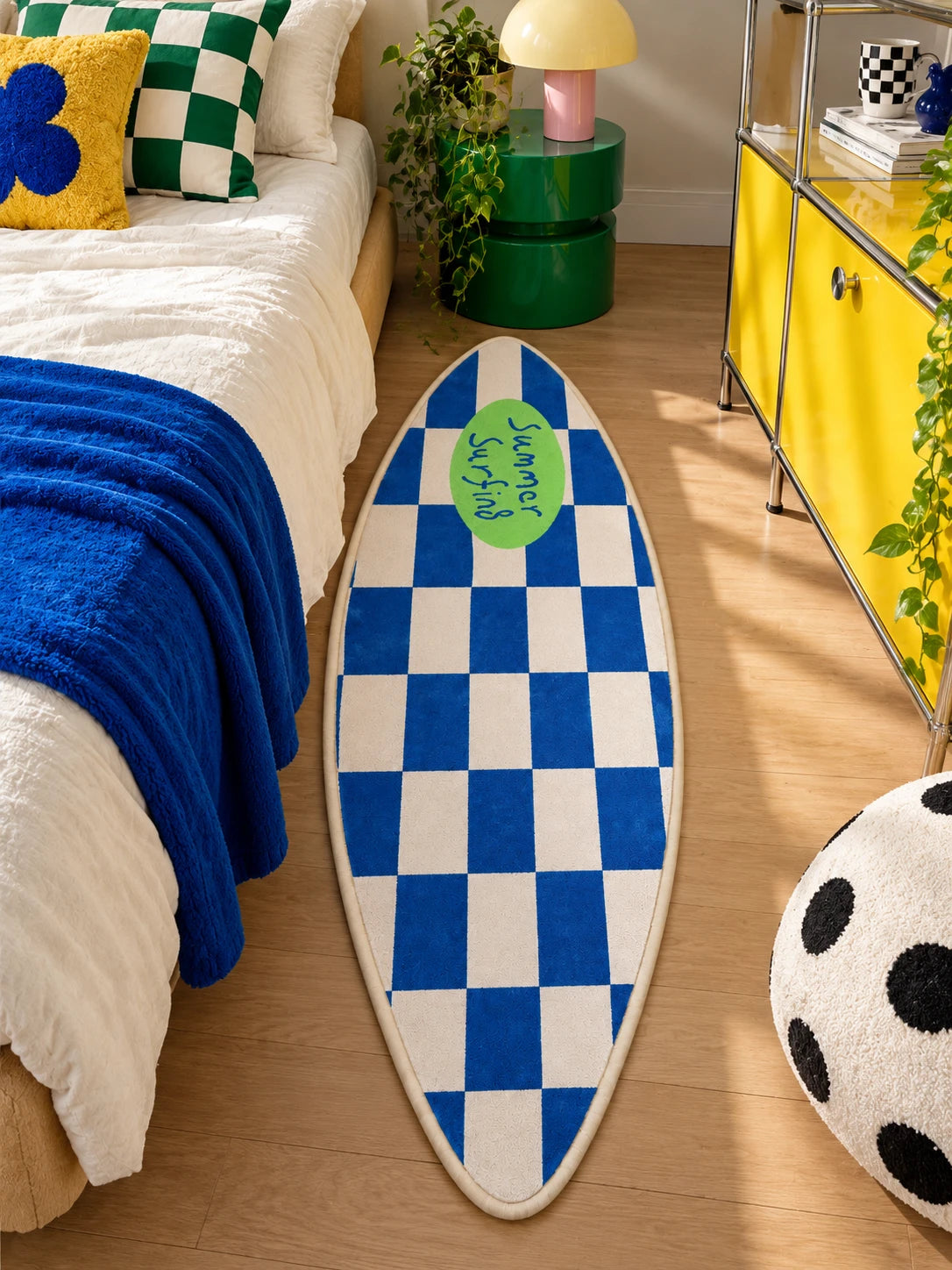 Surfboard runner rug alongside a bed with royal blue blanket and yellow metal cabinet