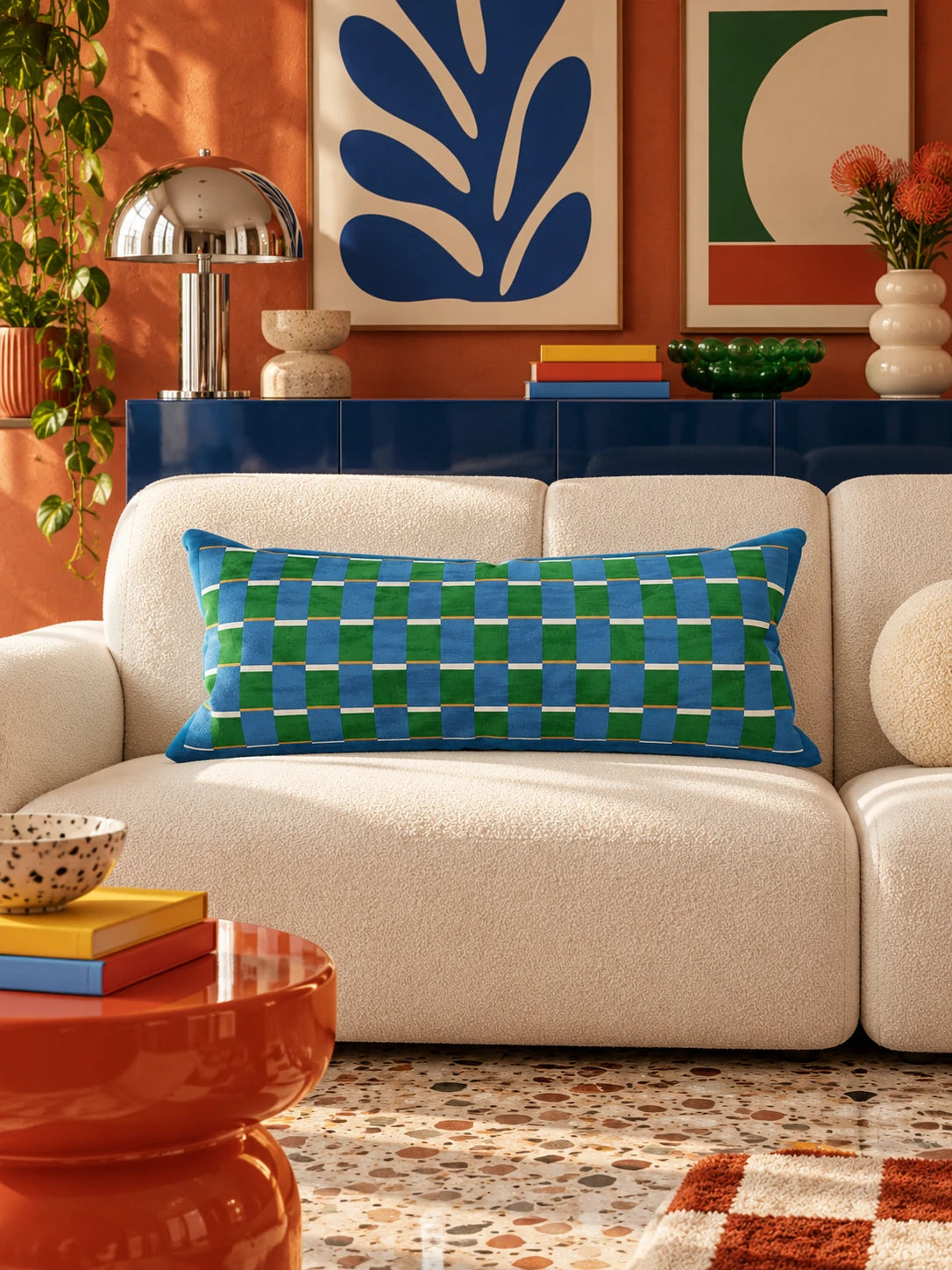 Blue and green check lumbar pillow on a cream boucle sofa below blue and green abstract prints