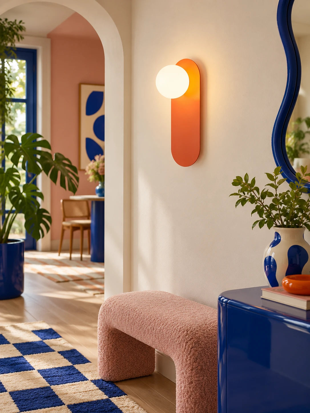 
Orange wall lamp glowing on a white wall above a pink boucle bench and blue sideboard