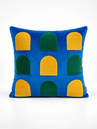 Cobalt velvet throw pillow with rows of yellow and green arched window shapes, studio shot
