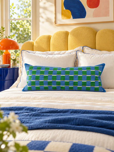 Blue and green check lumbar pillow on a white bed with a yellow scalloped headboard and a blue throw