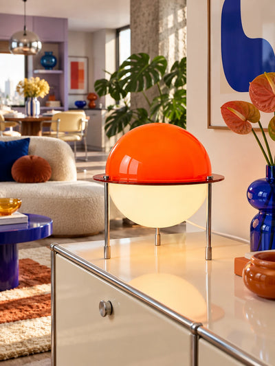 Orange space age lamp on a white storage cabinet with blue glass vase and anthurium stems