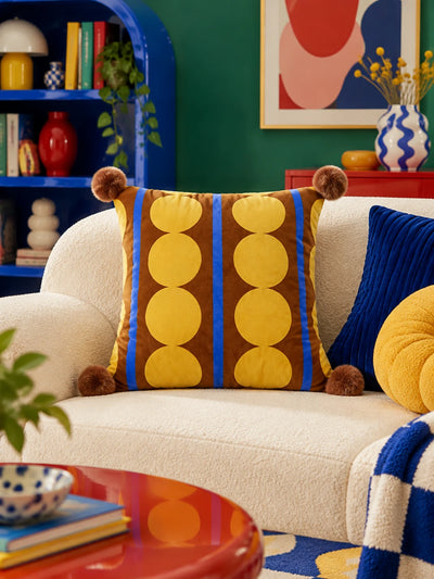 Brown dot stripe pompom pillow on a cream sofa beside a navy ribbed pillow and a red coffee table