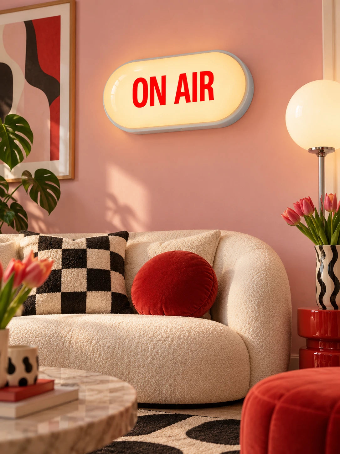 ON AIR sign on a pink wall above a cream boucle sofa with checkered pillow and tulips
