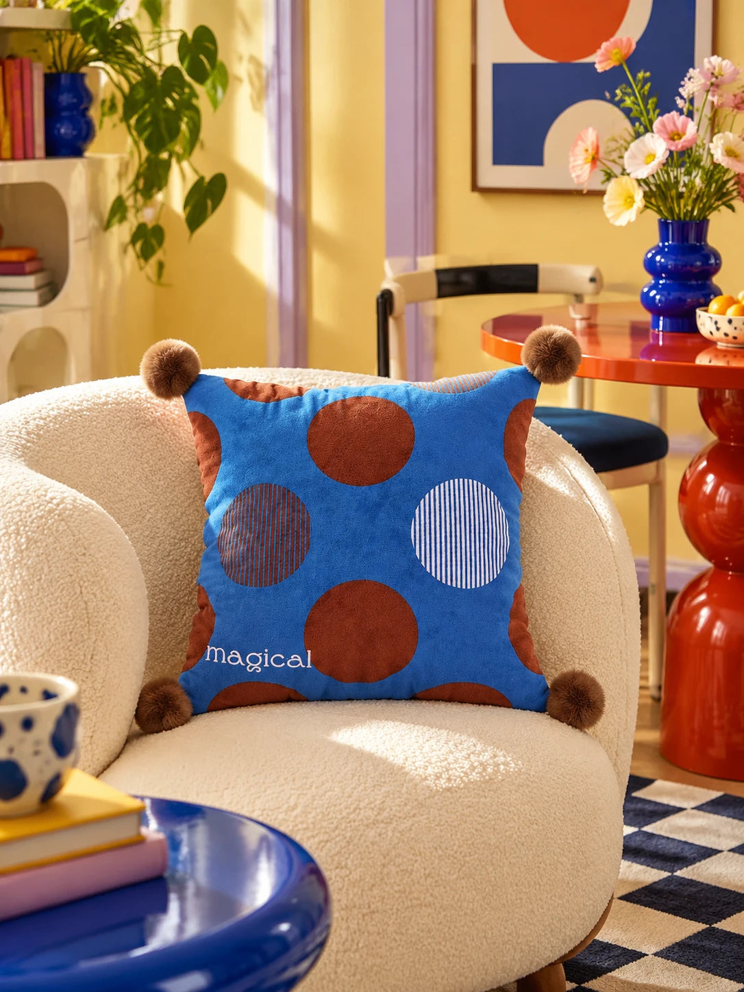 Cobalt polka dot pompom pillow on a cream boucle chair with a red bistro table in a yellow room
