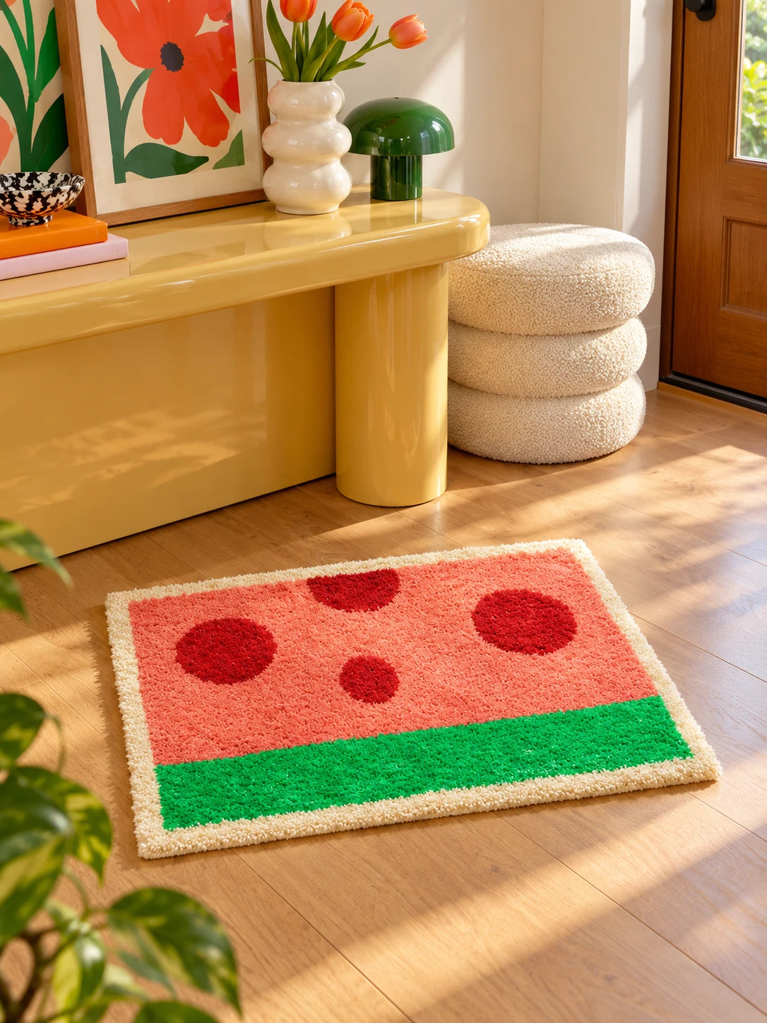 
watermelon flocked bath mat on a wood floor in a sunny entryway, in front of a glossy yellow console and stacked cream boucle poufs
