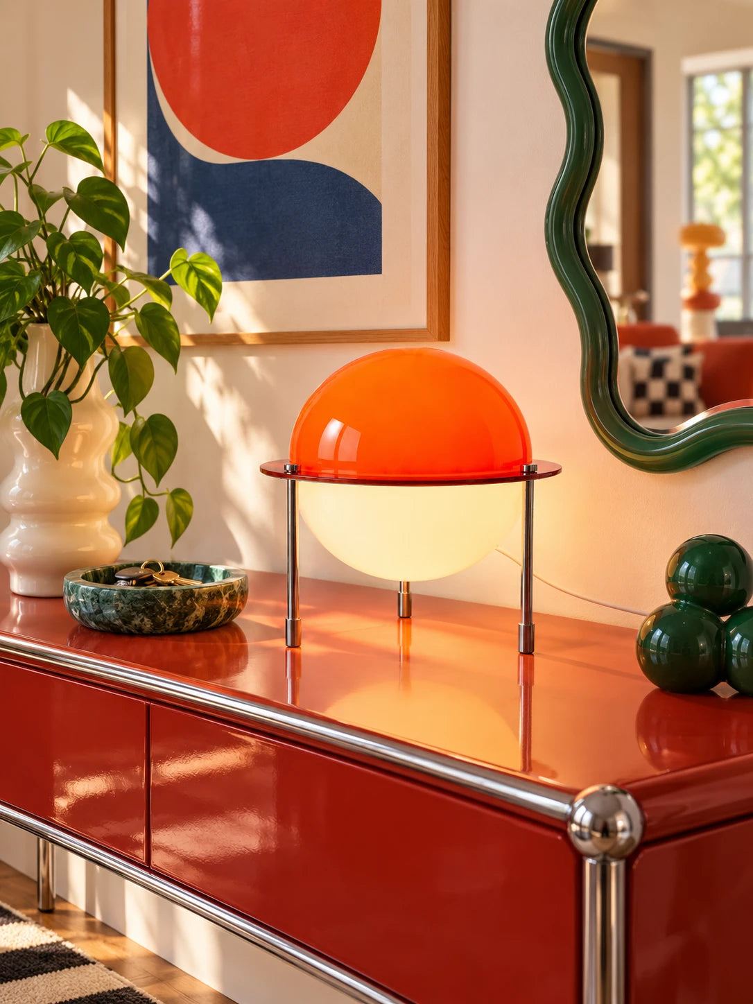 Space age lamp on a red console under a green wavy mirror with pothos plant