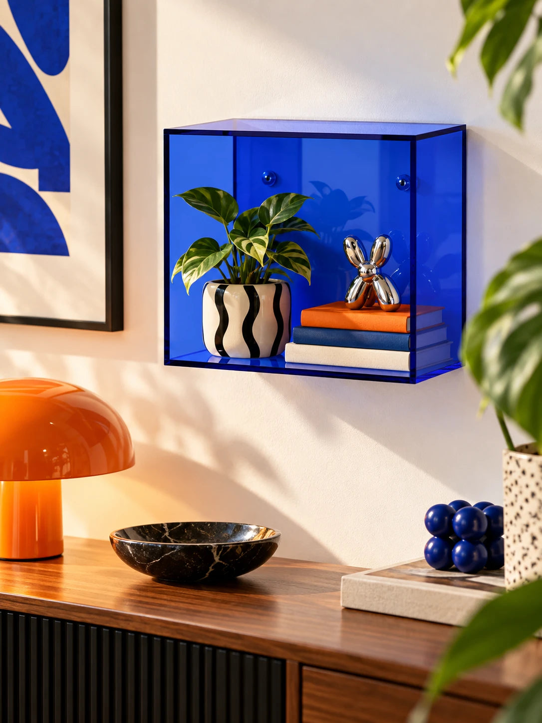 
blue acrylic wall display box holding a plant, books and a chrome figure above a sideboard