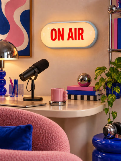 ON AIR light box over a podcast desk with microphone, chrome lamp and pink mug