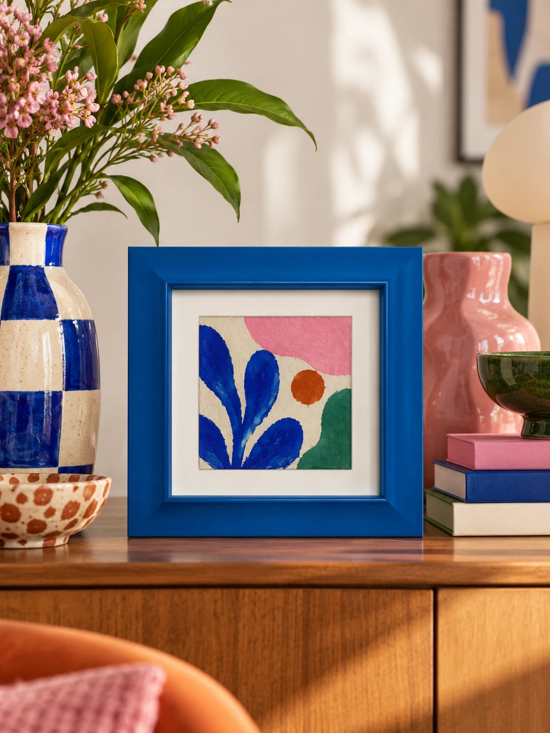 blue wood frame with leaf print standing on a dresser beside a checkered vase