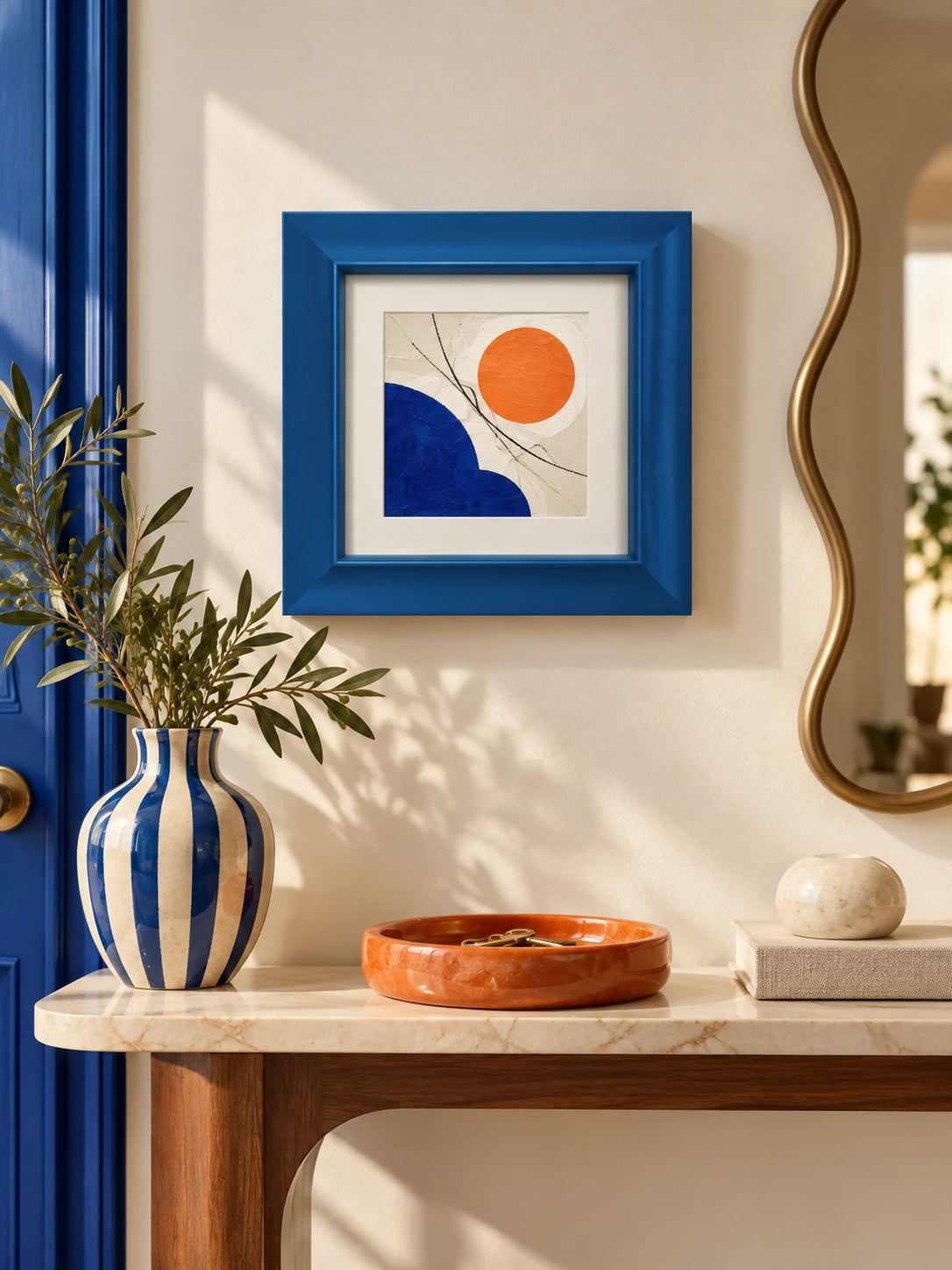 blue wood picture frame above a marble console with a gold wavy mirror