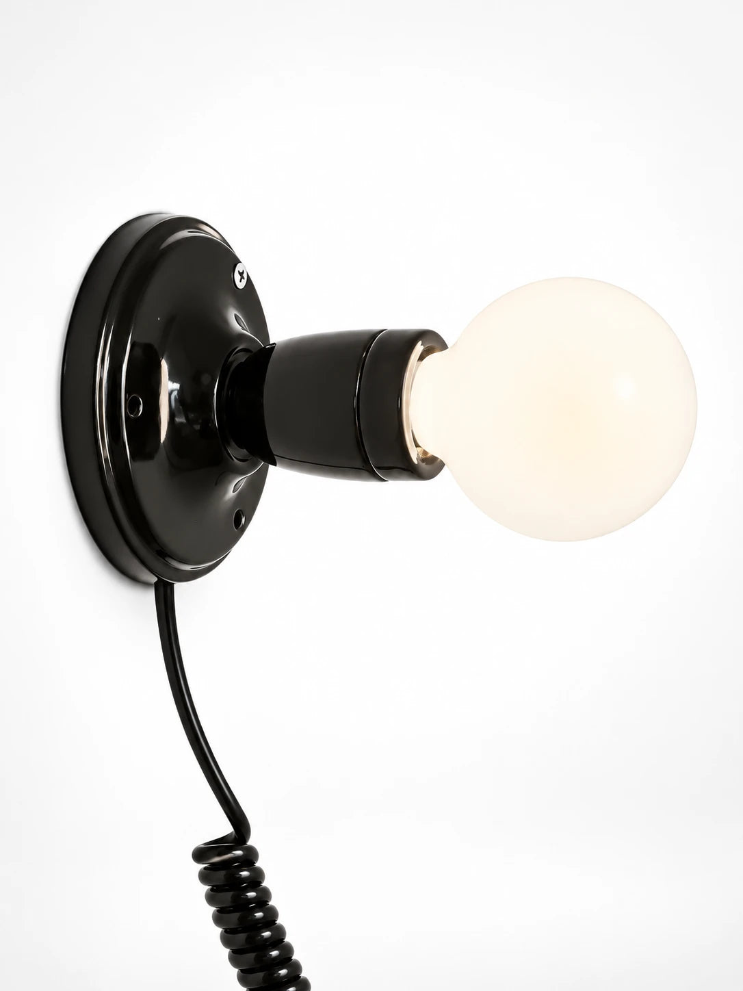 
black ceramic wall light with an opal globe bulb and coiled black cord, studio shot on white