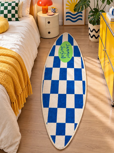 Blue checkerboard surfboard rug beside a bed with mustard fringe throw and cream drum nightstand