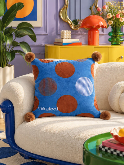 Cobalt and brown polka dot pompom pillow on a cream sofa with a cobalt frame in a lilac room
