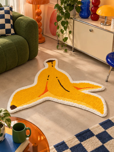 Yellow banana peel mat on concrete floor by a green sofa and orange bobbin floor lamp