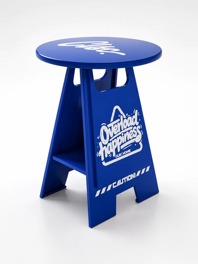 bright blue caution-sign shaped side table with white graphics, a cutout handle, and a low inner shelf